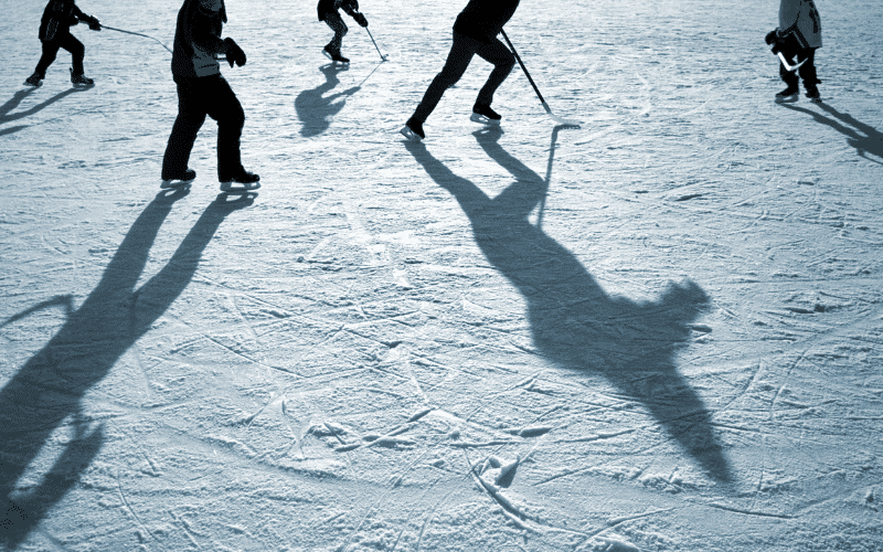 A group of players on a frozen pond, using curved sticks to propel a small disk across the ice, surrounded by cheering spectators